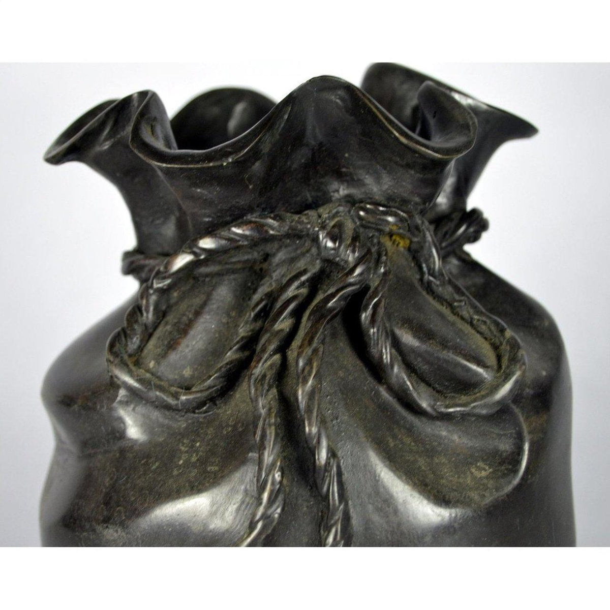 Close-up of a dark ceramic vase shaped like a tied bag, called the Bronze Pouch, on a tabletop.