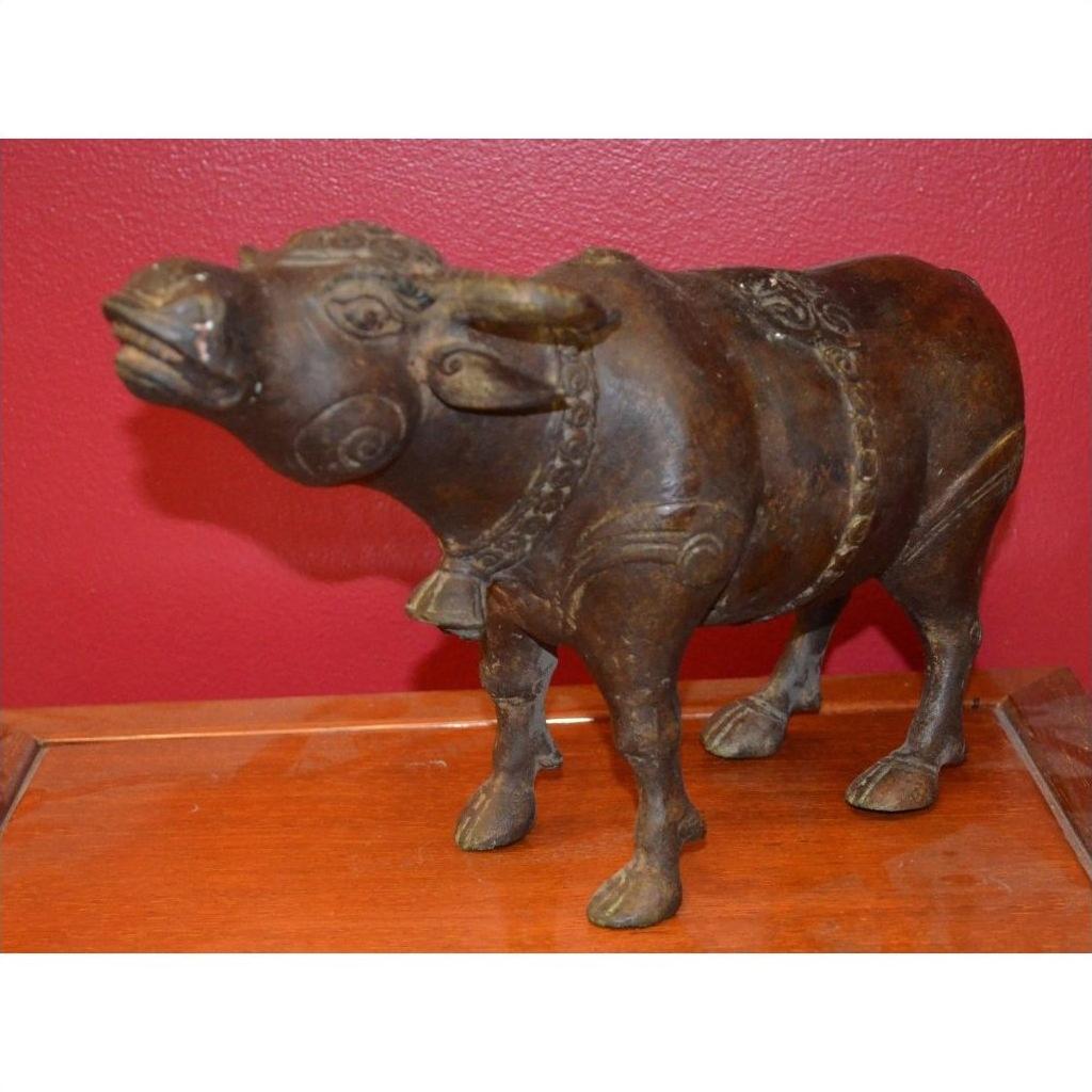 Close-up of a detailed bull sculpture made of metal on a wooden surface with a red wall background.
