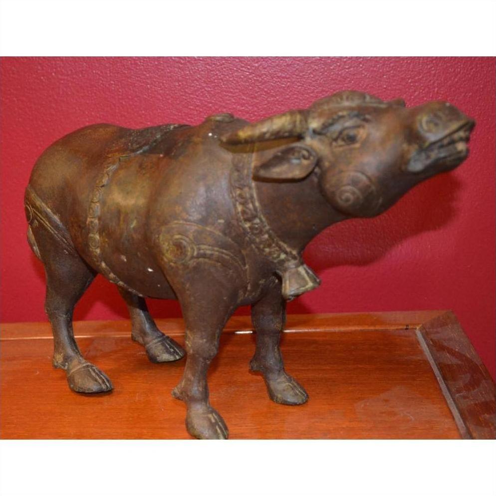 Bronze bull sculpture with detailed features on a wooden surface, set against a red wall.