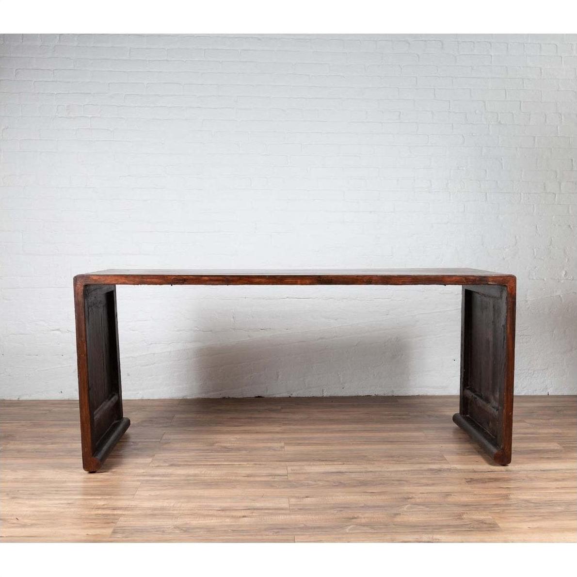 Dark wood Burmese vintage waterfall console table with scrolling feet against a white brick wall.