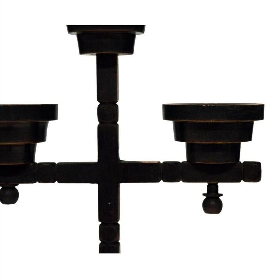 Close-up of a black metal candle holder with three arms and minimalist geometric design on white background.