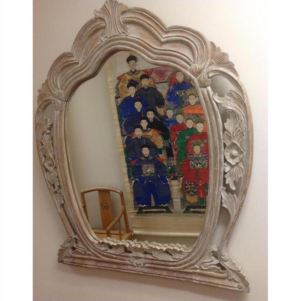 Brown carved wooden mirror reflecting portrait of people in traditional attire, wooden chair visible in background.