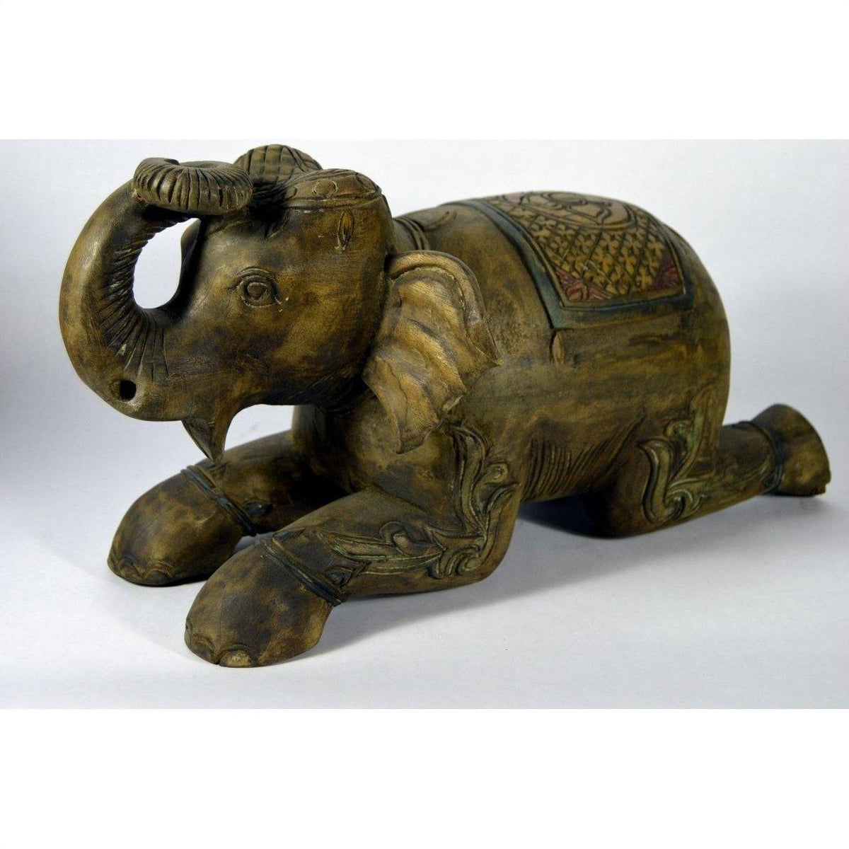 Brown wooden Chiang Mai hand carved elephant figurine with ornate carvings, close-up on plain background.