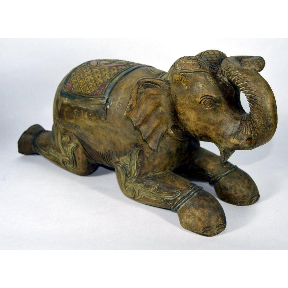 Close-up of hand-carved wooden elephant figurine from Chiang Mai, kneeling with trunk raised, decorative patterns visible.