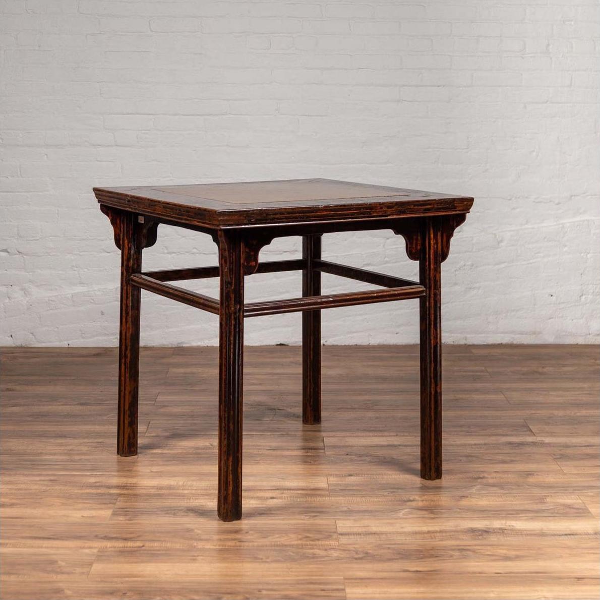Brown elmwood Chinese 19th c. center hall table with Ming Dynasty stone inset by a white brick wall on wood flooring.