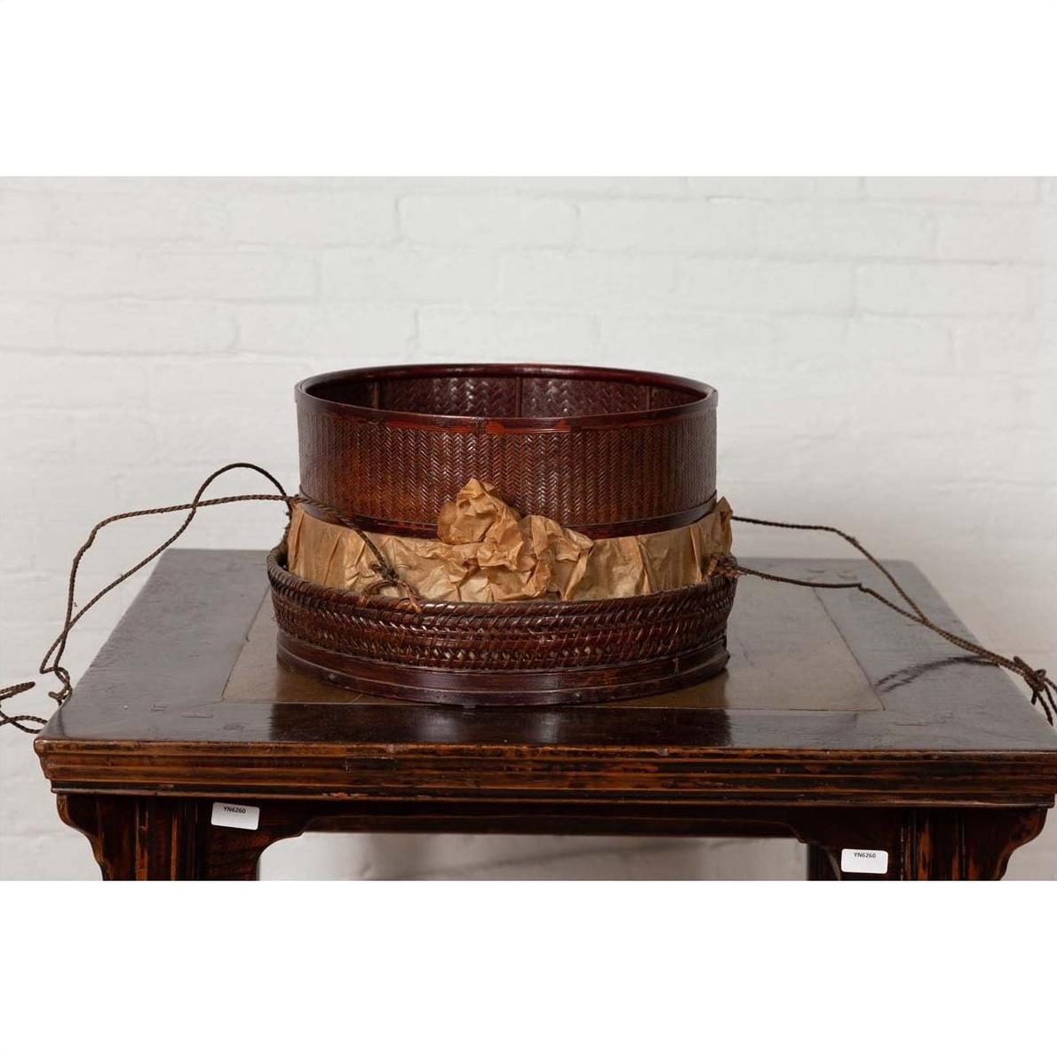 Black wood Chinese 19th century tiered food basket with stacking parts on a dark wood table, white brick wall background.