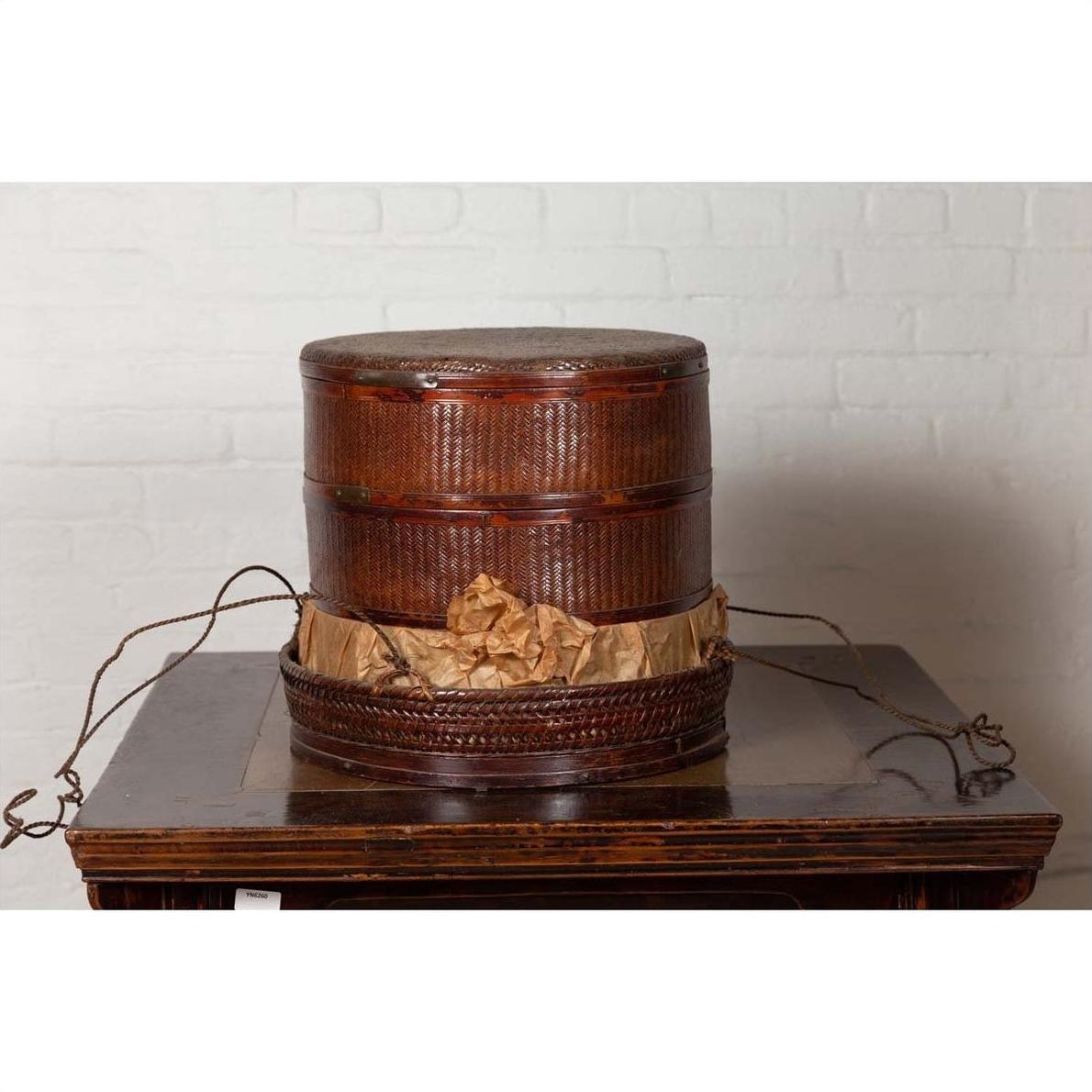 Brown wood tiered food basket with stacking sections on dark table, white brick wall background, 19th century Chinese style.