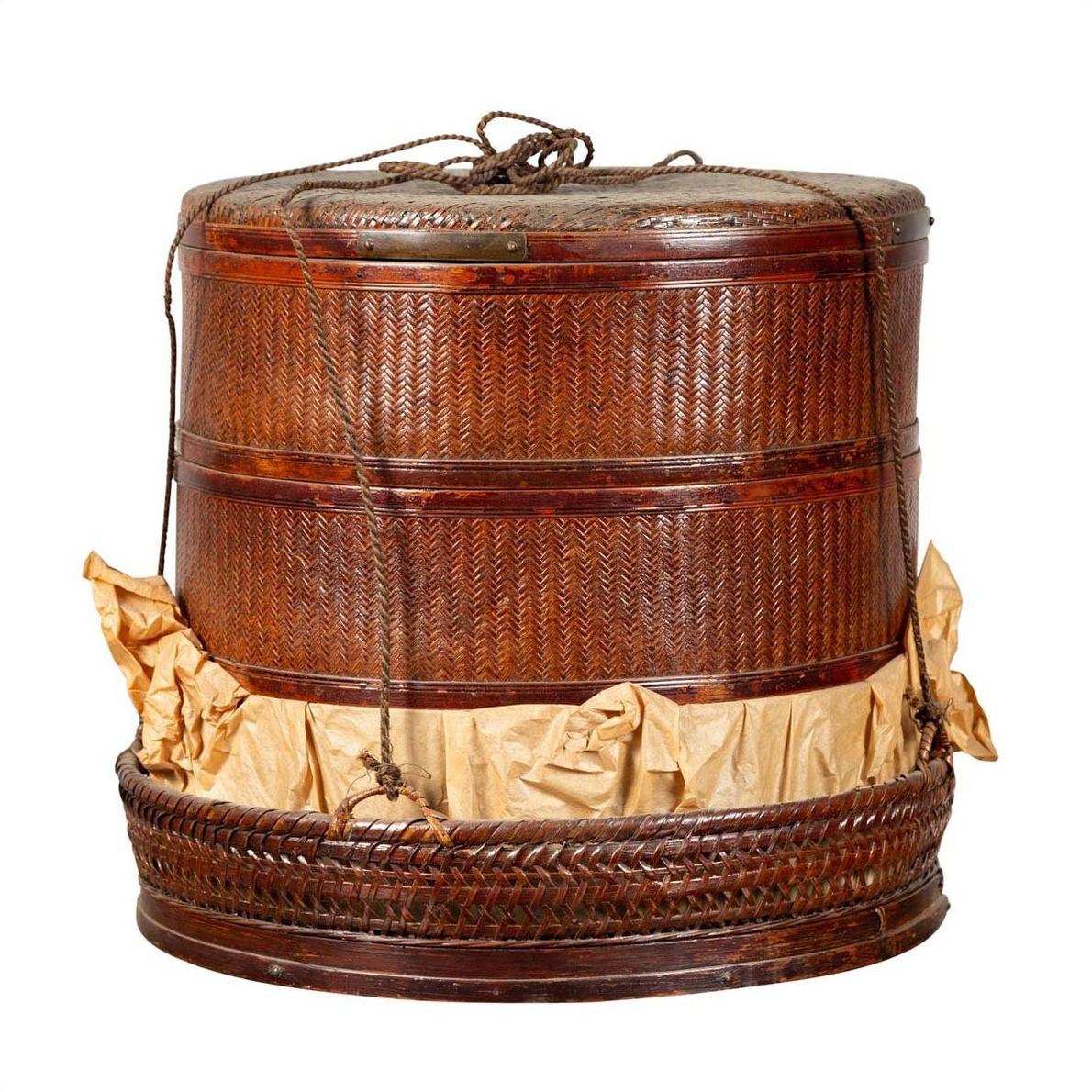 Brown woven Chinese 19th century tiered food basket with stacking parts, lid, and rope handles on a plain background.
