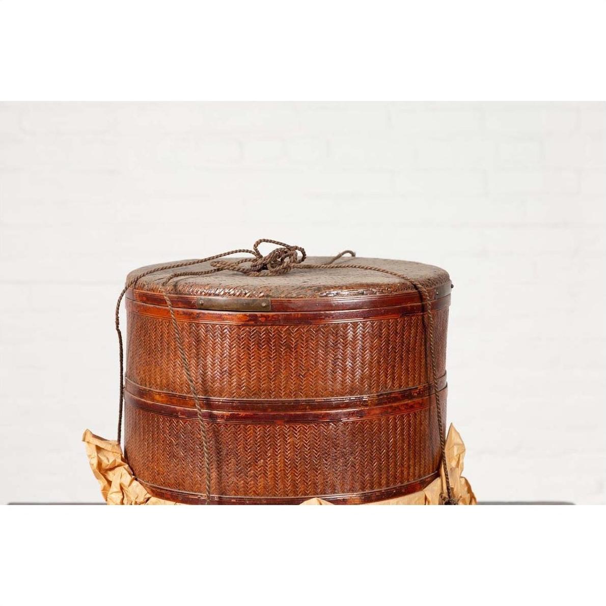 Brown wood Chinese tiered food basket with stacking parts and lid on crumpled paper, white background.