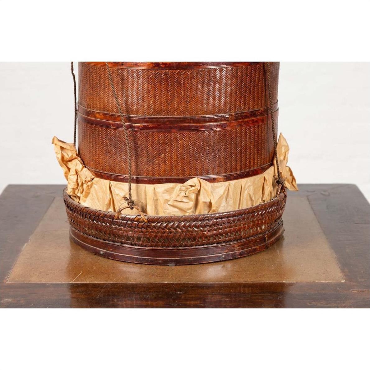 Close-up of a brown Chinese 19th century tiered food basket with stacking parts and paper, on a wooden surface.