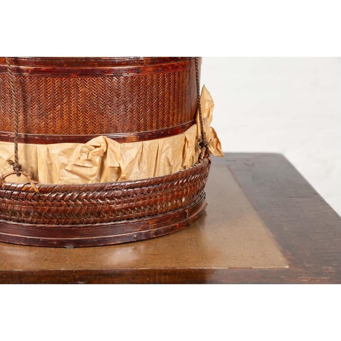 Close-up of a brown wood Chinese 19th century tiered food basket with stacking parts and crumpled paper on dark wood.