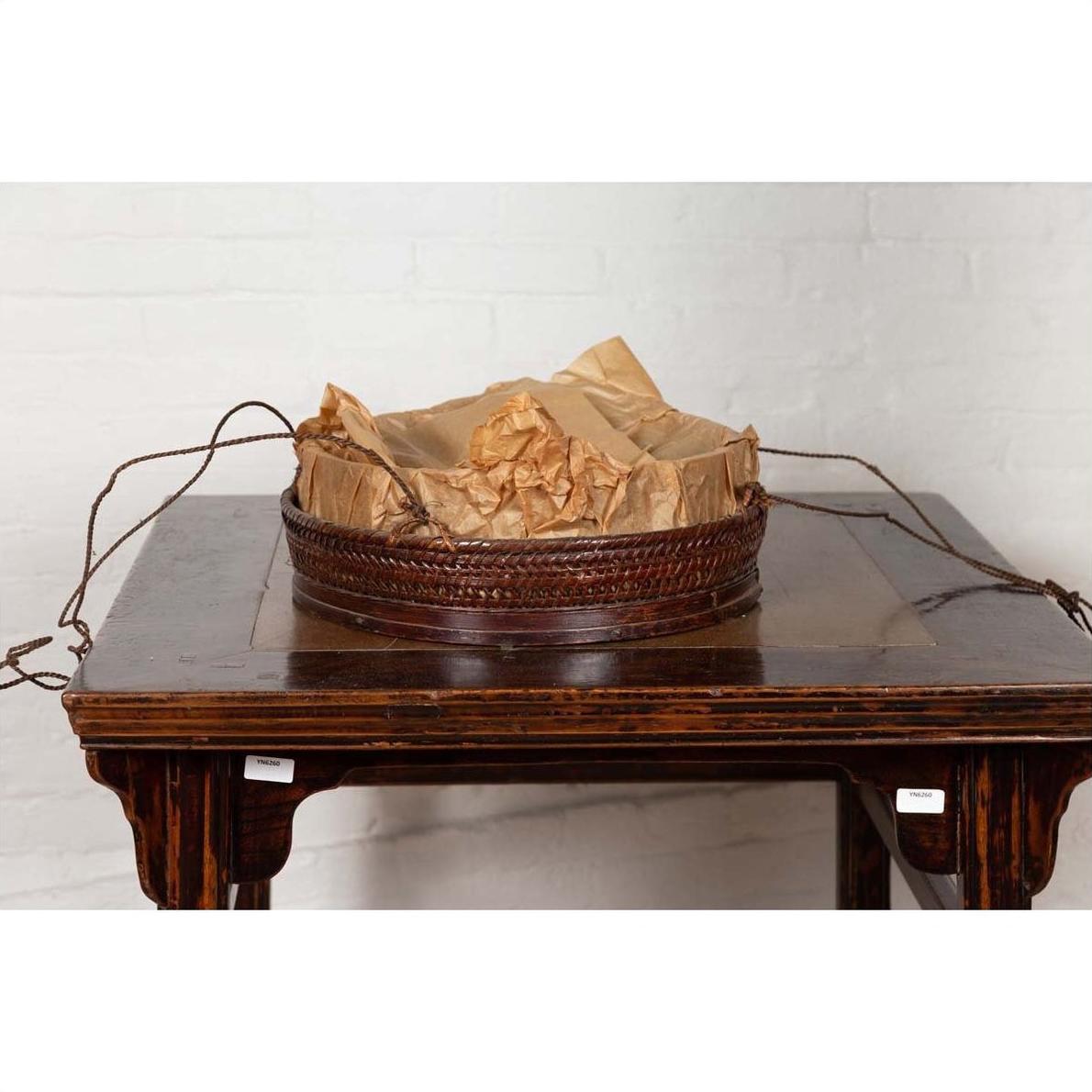 Dark wood Chinese 19th century tiered food basket with stacking parts on a dark wood table against a white brick wall.