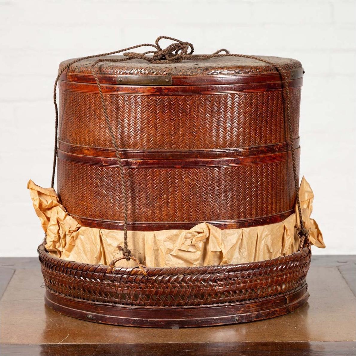 Brown wood Chinese tiered food basket with rope handles, lid, stacking sections, and crumpled paper at base.