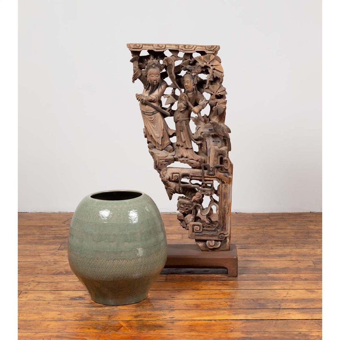 Green ceramic vase and Chinese antique 1900s hand carved wood corbel with deities on wooden floor.