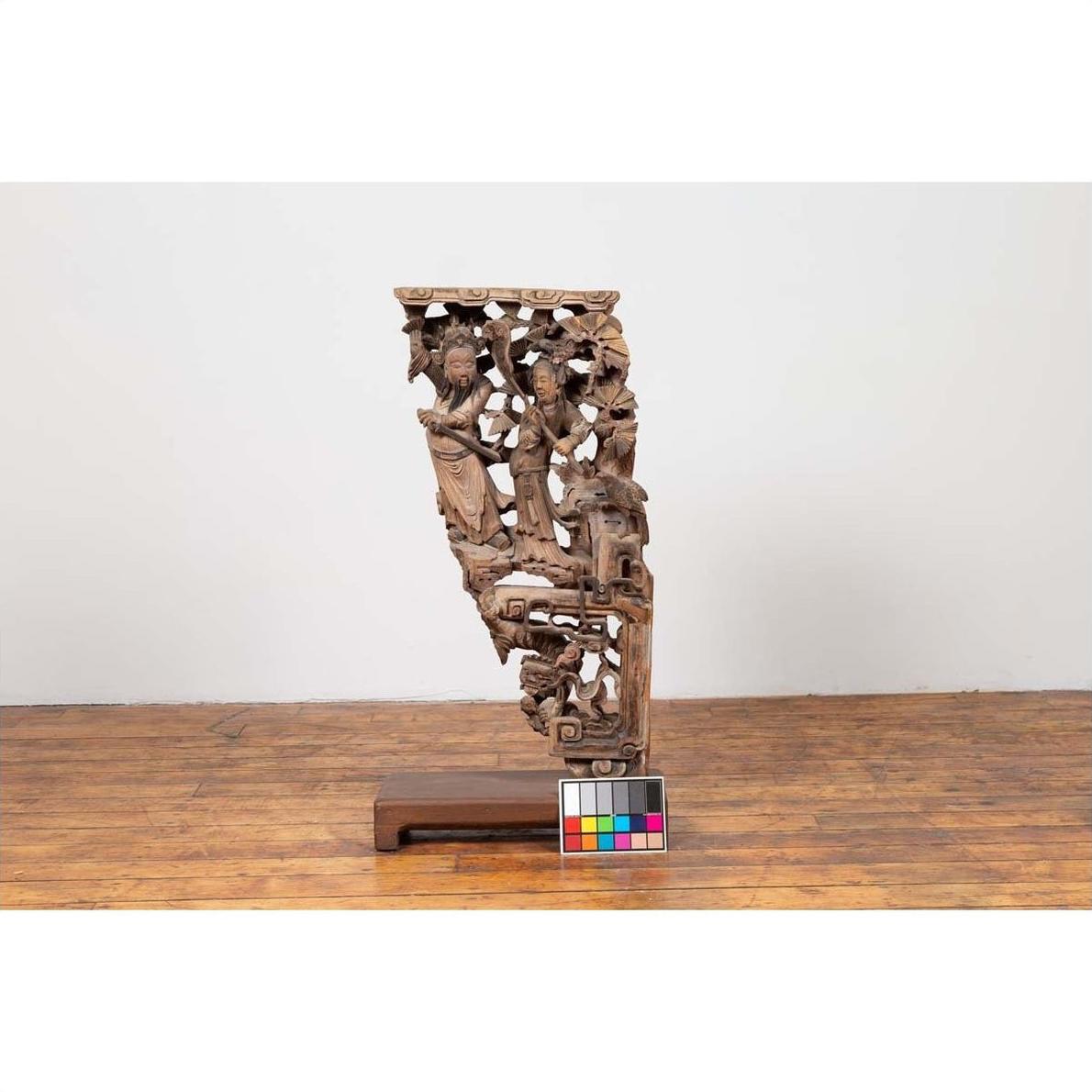 Brown wooden hand carved corbel with deity figures from 1900s China, mounted on base, next to color calibration chart.