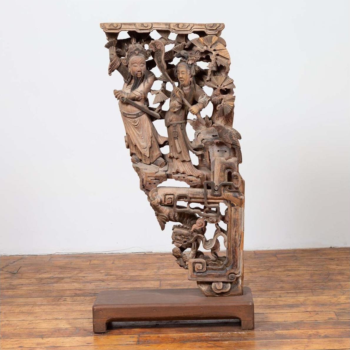 Brown wood hand carved Chinese corbel with deity figures and detailed floral, geometric motifs on wooden base, close-up.