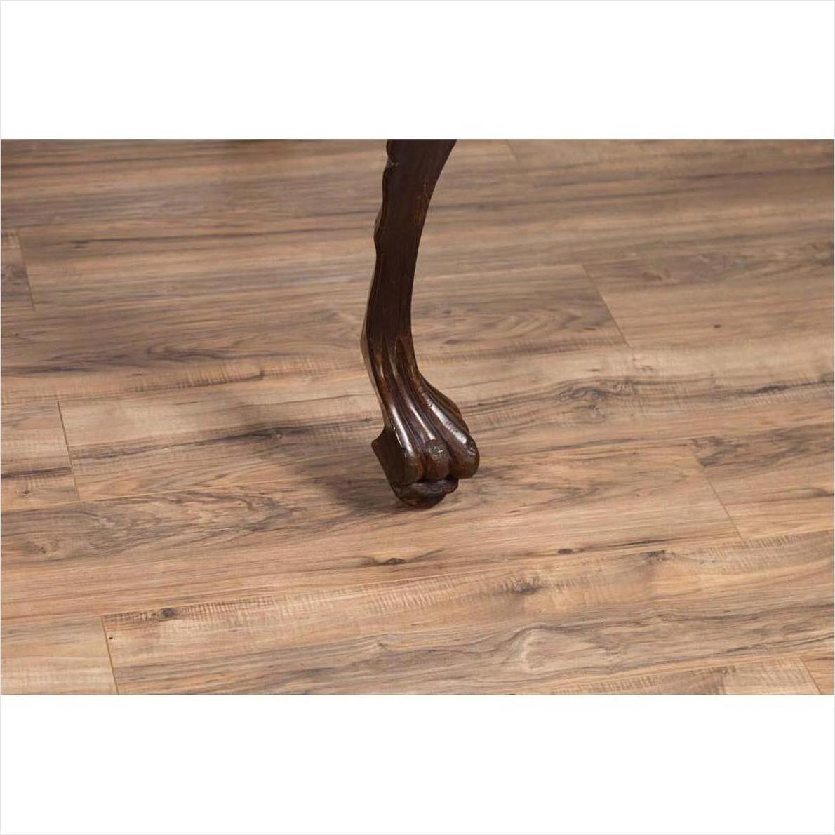 Close-up of dark wood cabriole leg with carved animal paw detail on light floor, classic antique table style.