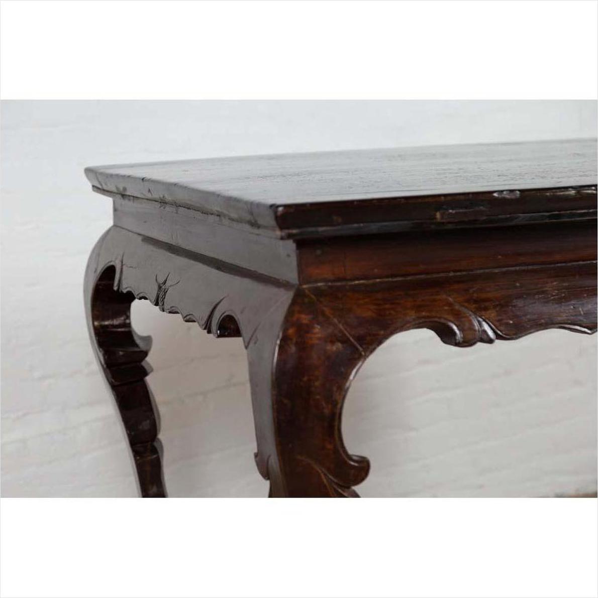 Black lacquered wood hall table with cabriole legs, set indoors against a light brick wall.