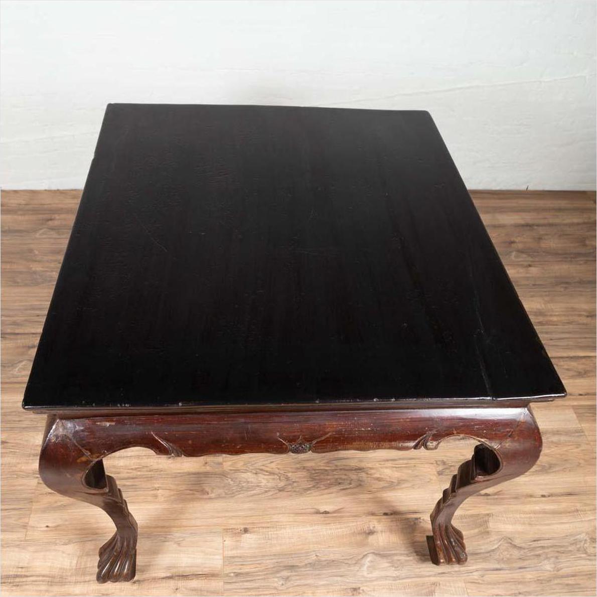 Black lacquered wood center hall table with cabriole legs on a wooden floor against a white wall indoors.