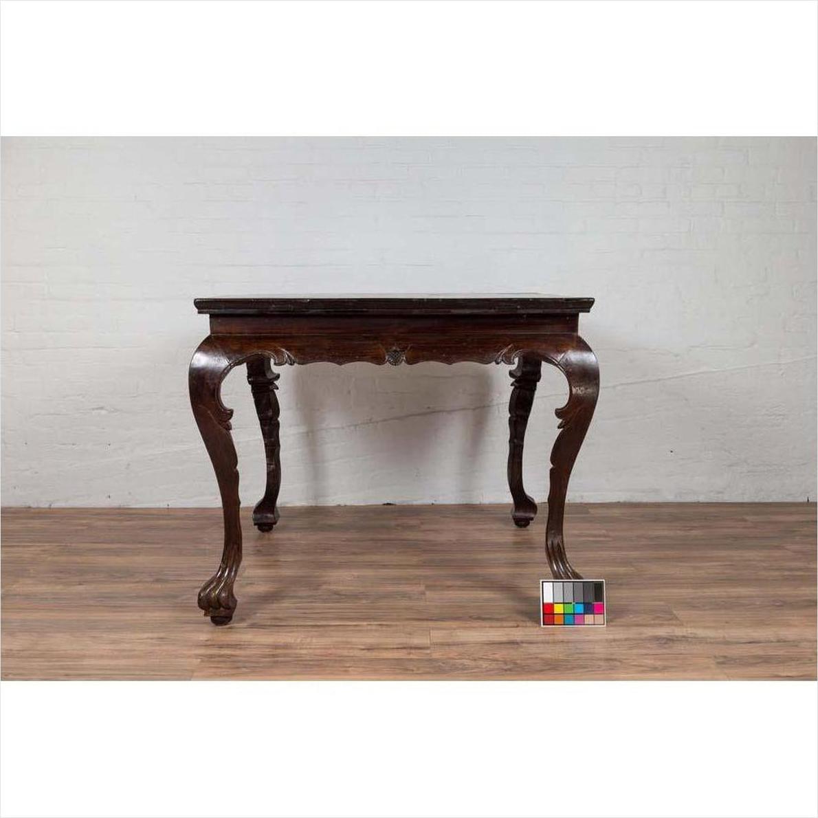 Black lacquered wood center hall table with cabriole legs on a wood floor next to a white brick wall indoors.
