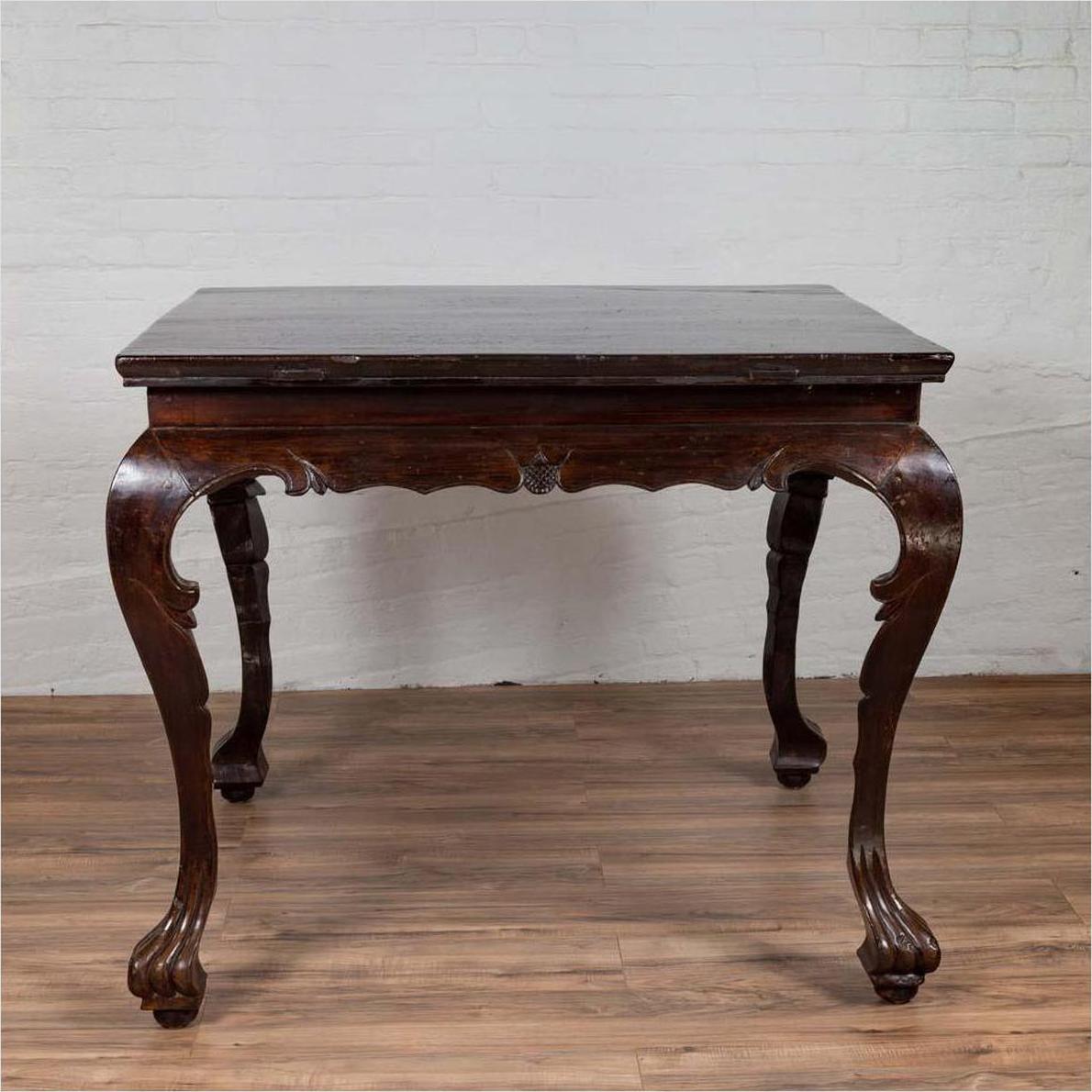 Black lacquered wood hall table with cabriole legs, placed on wooden floor next to a white brick wall indoors.