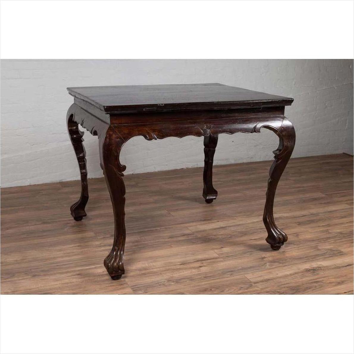 Black lacquered wood hall table with cabriole legs on a wood floor against a white brick wall indoors.