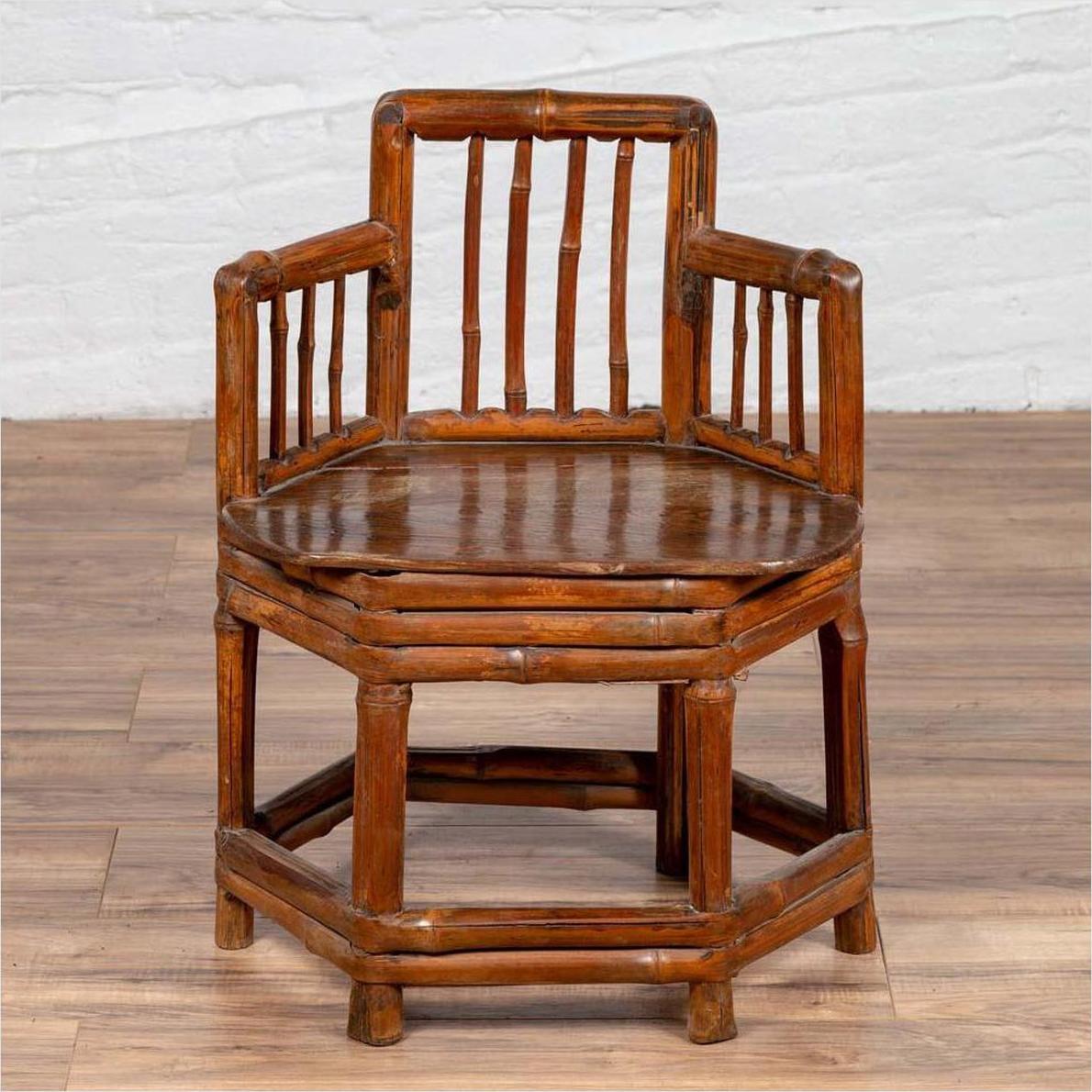Brown bamboo corner chair with hexagonal base on wooden floor next to a white brick wall indoors.