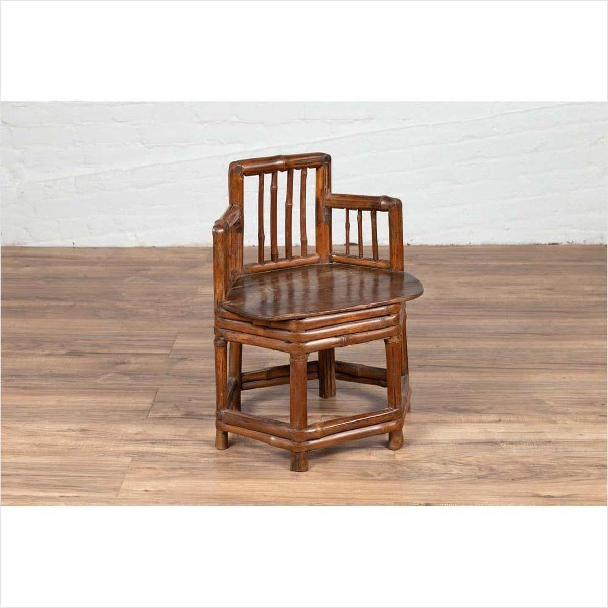 Brown bamboo child's corner chair with hexagonal base on wooden floor next to a white brick wall indoors.