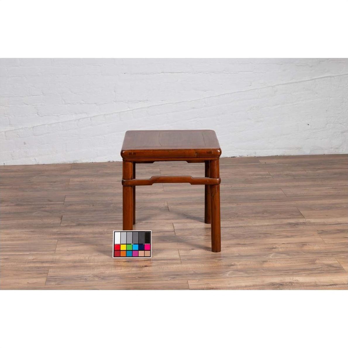 Brown wood Ming style side table with humpback stretcher, antique finish, on wood floor against a white wall.