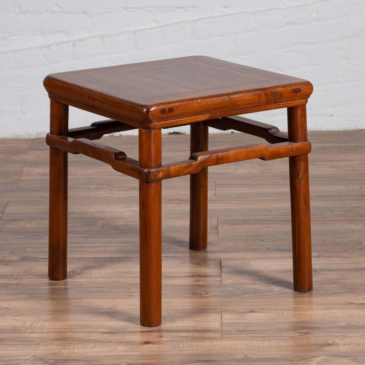 Brown wood Chinese Ming style side table with humpback stretcher on wood floor by white brick wall.