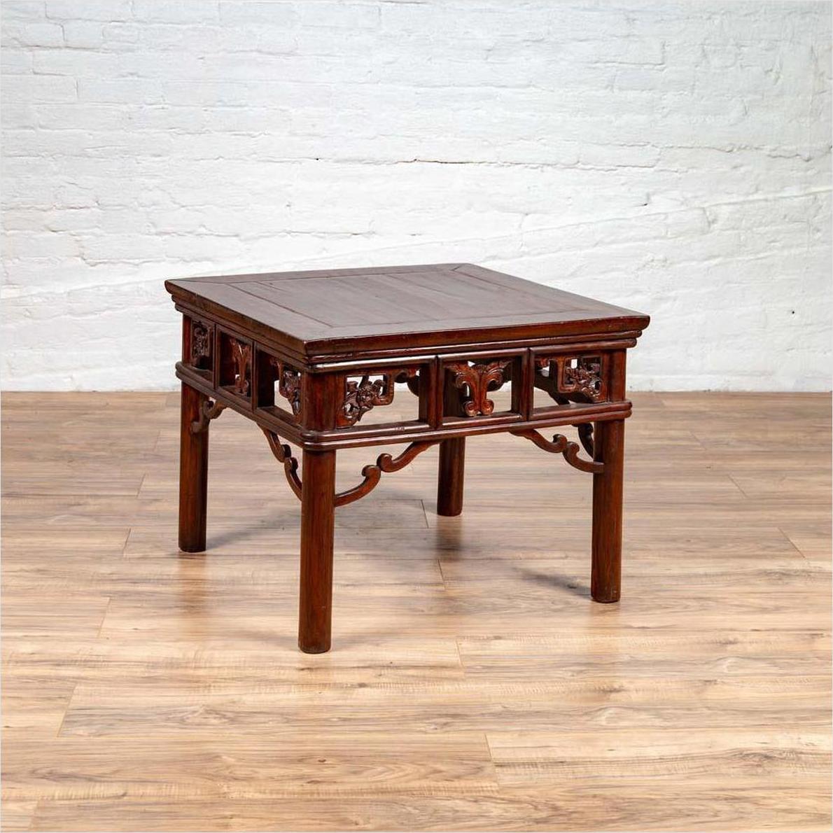 Dark wood Chinese antique side table with open fretwork design on wooden floor against white brick wall.
