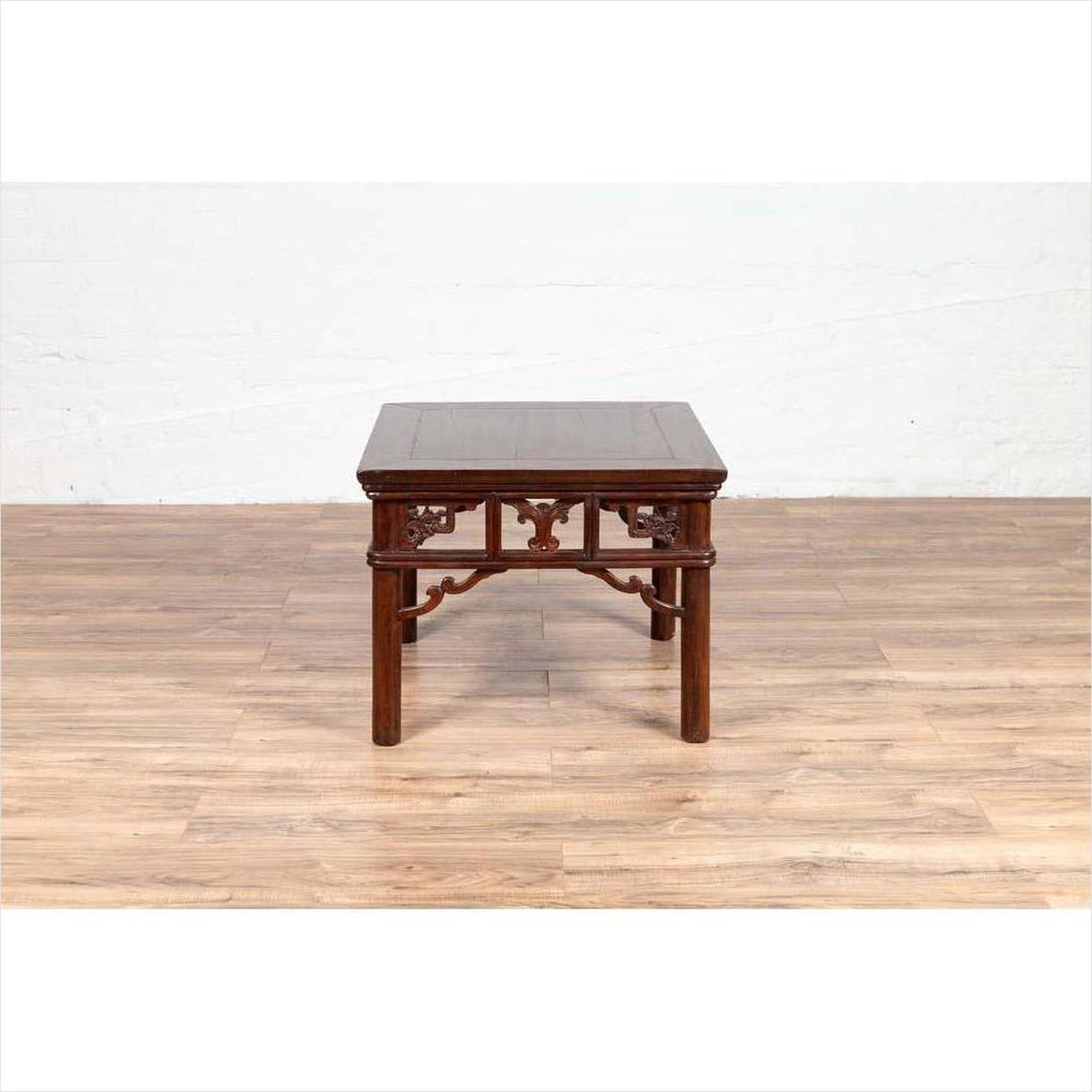 Dark wood Chinese antique side table with open fretwork design on light wood floor, white wall background.