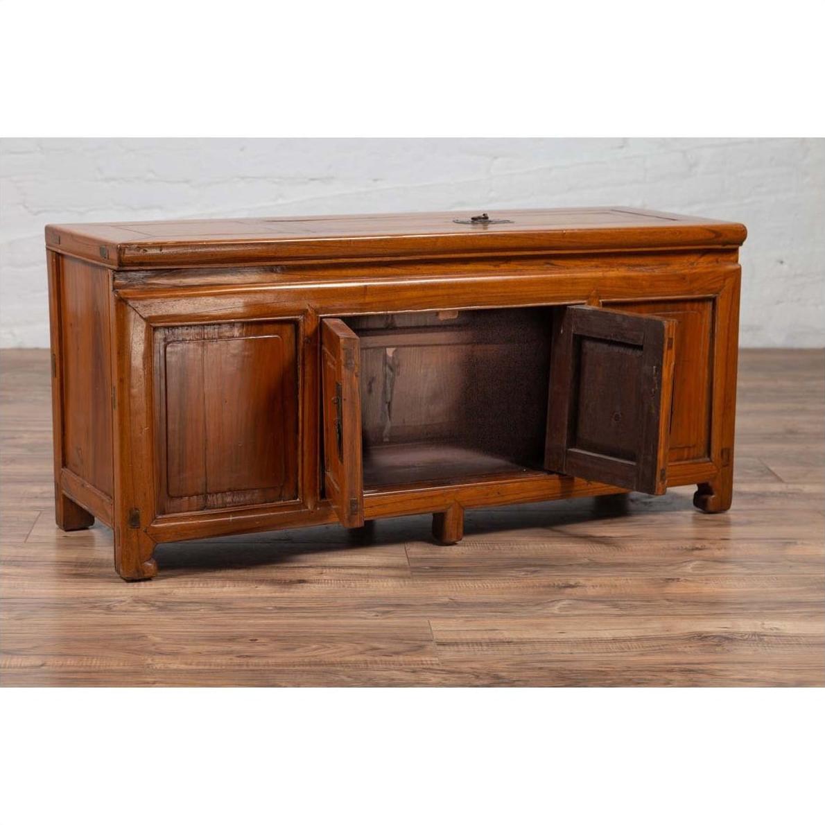Brown wood two-door Chinese buffet with faux doors and removable panel on hardwood floor by white brick wall indoors.
