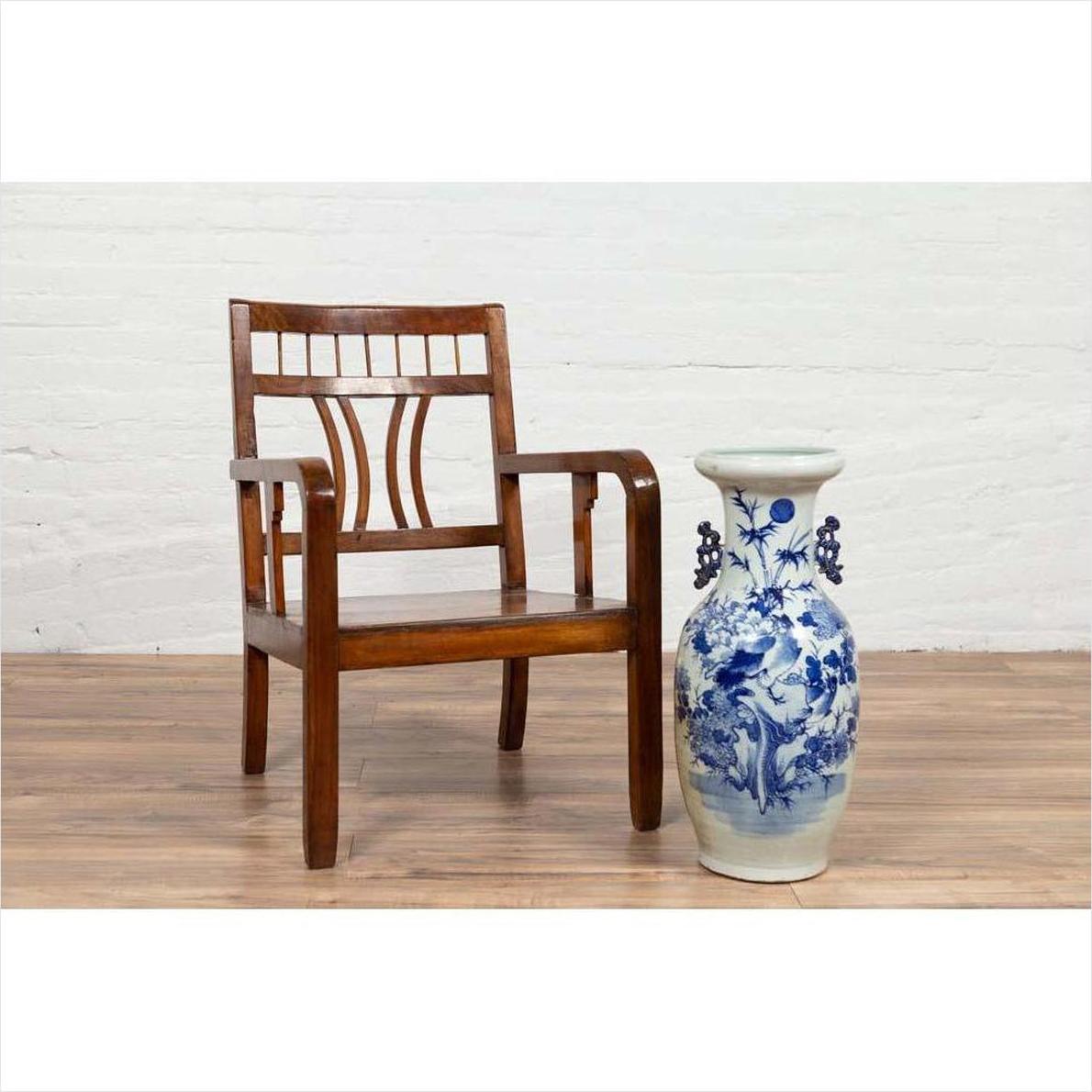 Brown elmwood Chinese Art Deco armchair with pierced and curved design beside white and blue ceramic vase on wood floor.