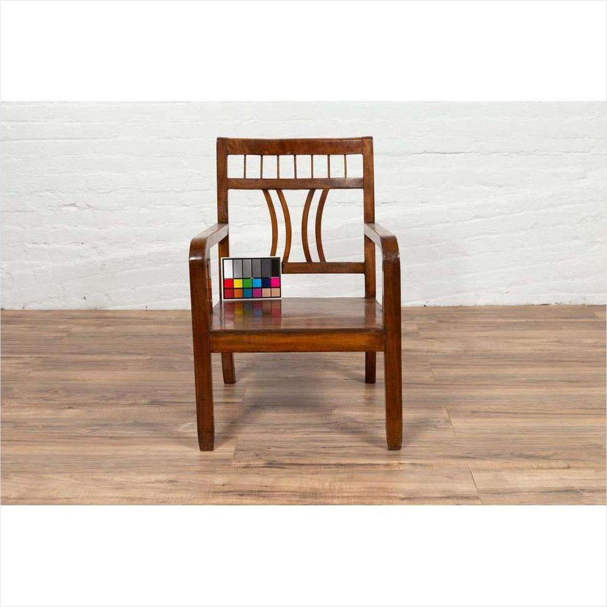Brown elmwood Chinese Art Deco armchair with geometric backrest, color card on seat, on wood floor, white brick wall.