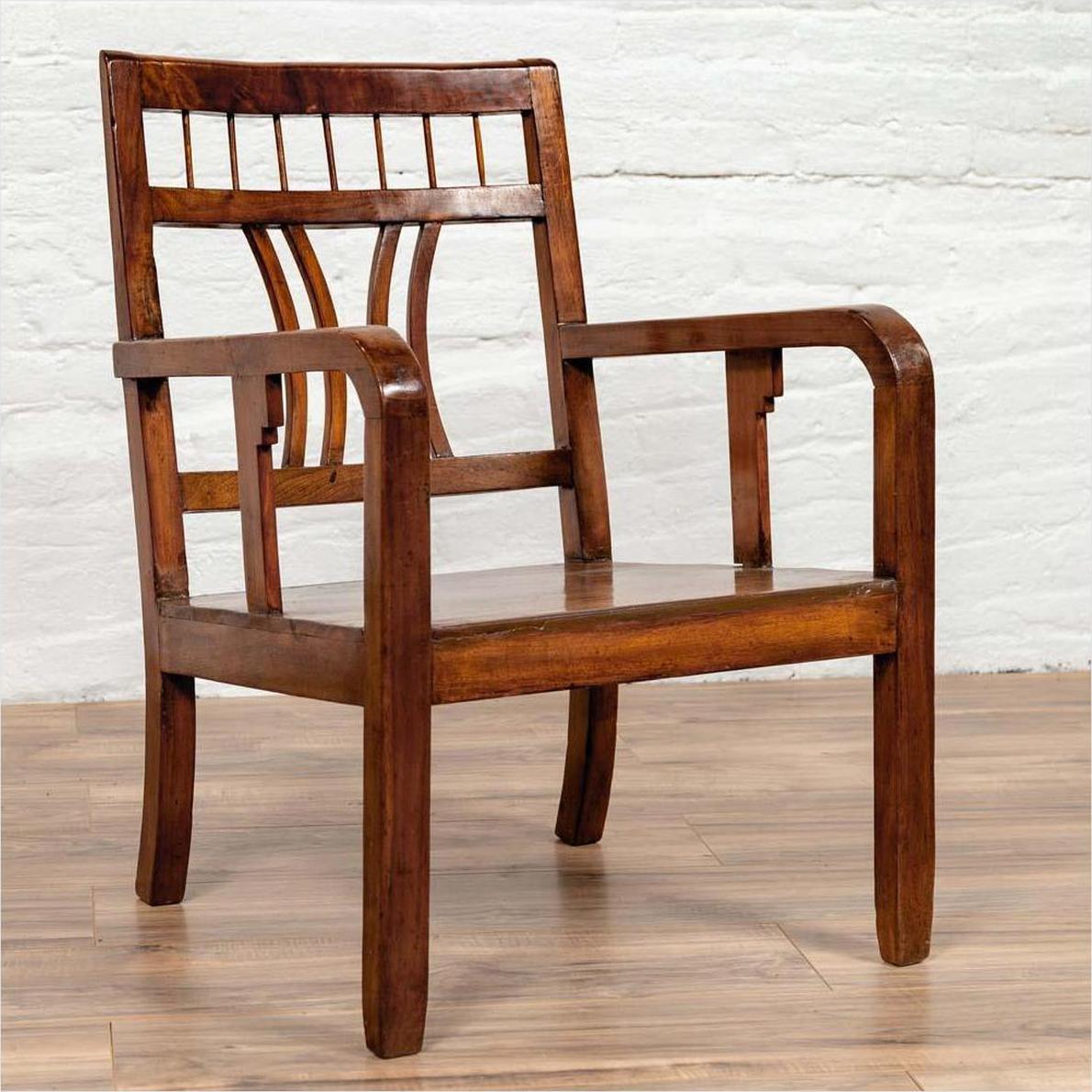 Brown elmwood Chinese Art Deco armchair with pierced curved back, positioned by a white brick wall on wood flooring.