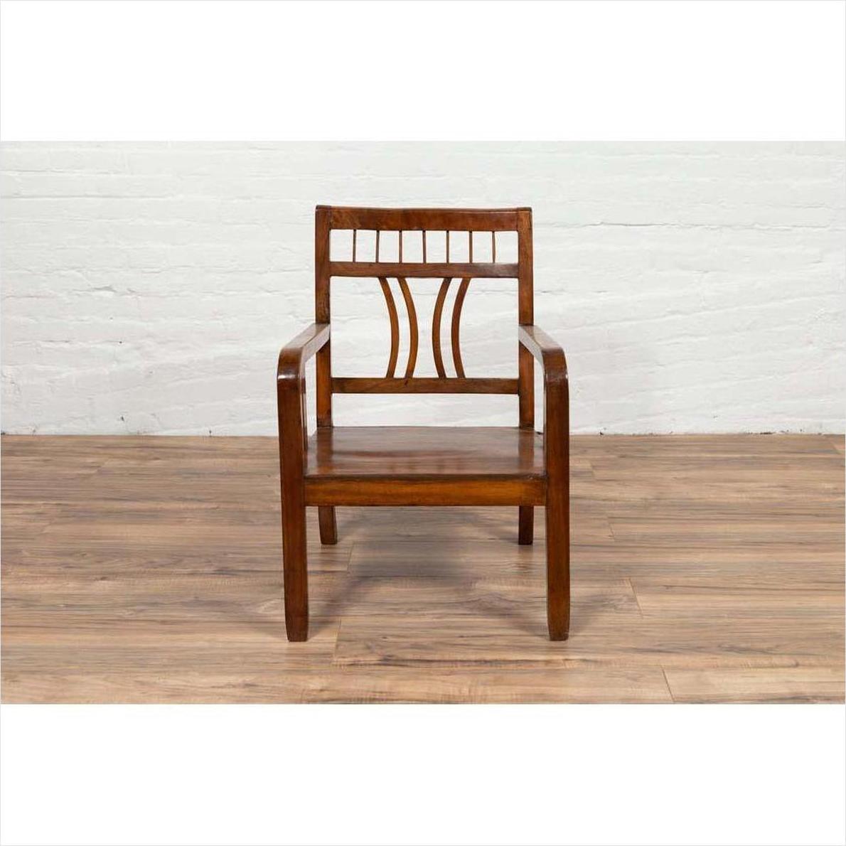 Brown elmwood Chinese Art Deco 1950s armchair with pierced and curved design on wooden floor, white brick wall background.