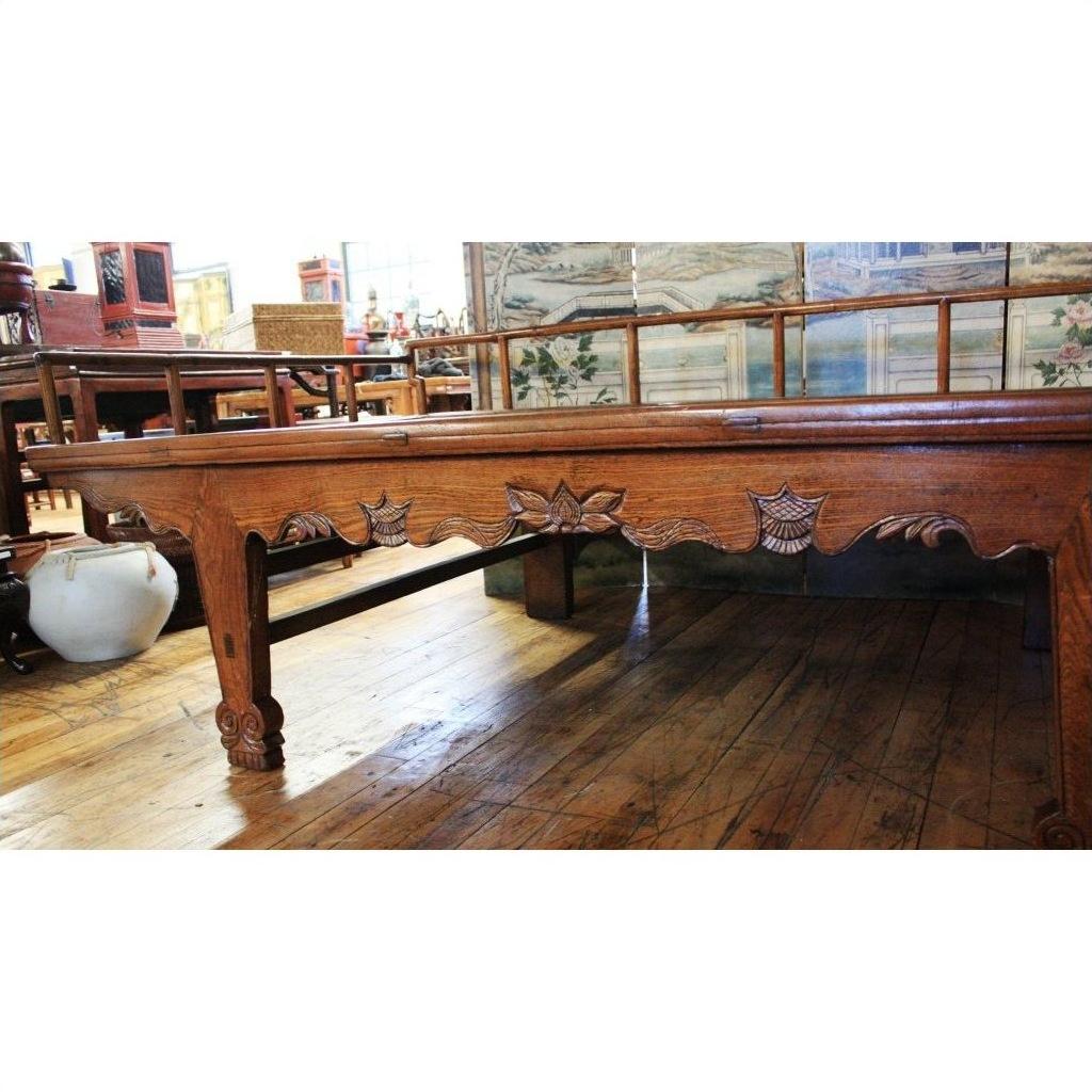 Dark wood Chinese daybed with carved floral sides, set on a wooden floor inside an antique store.