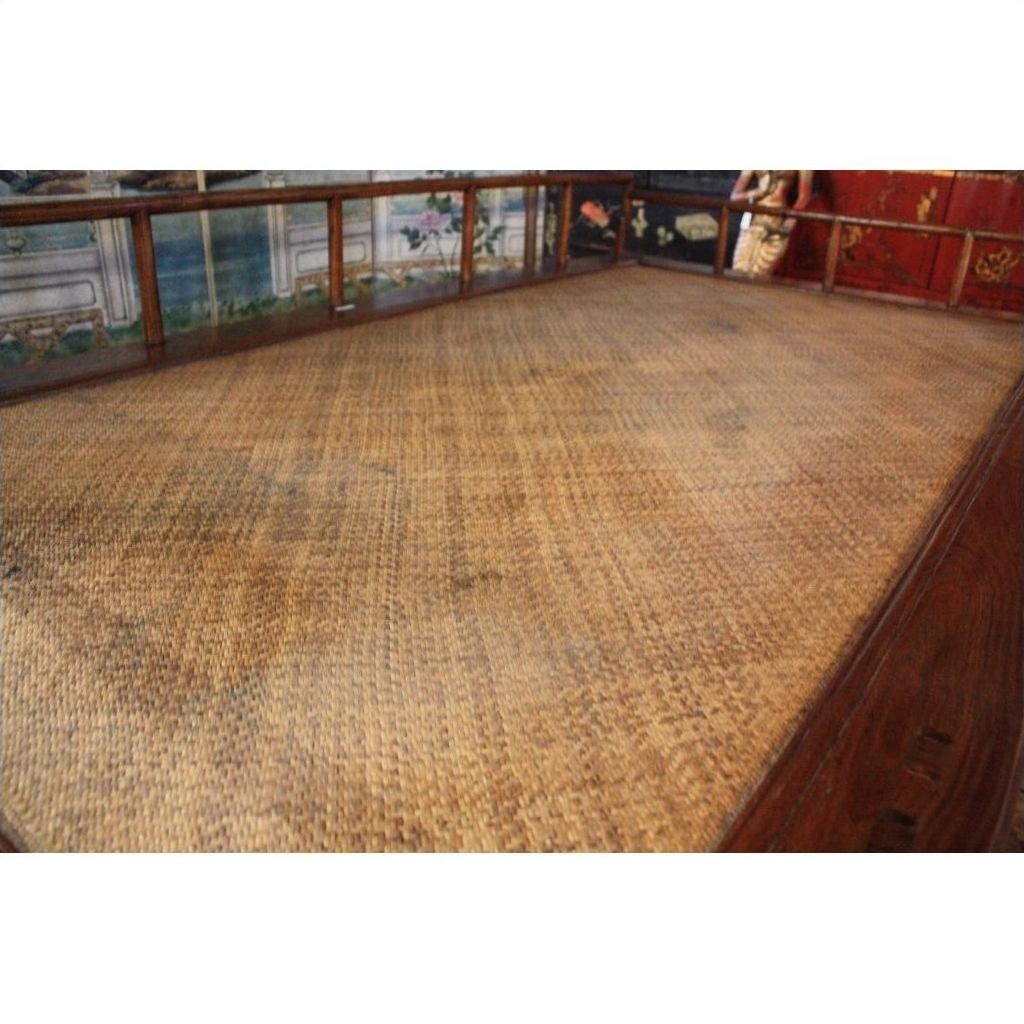 Brown wooden Chinese daybed with woven bamboo or rattan seat and decorative backrest, indoors.