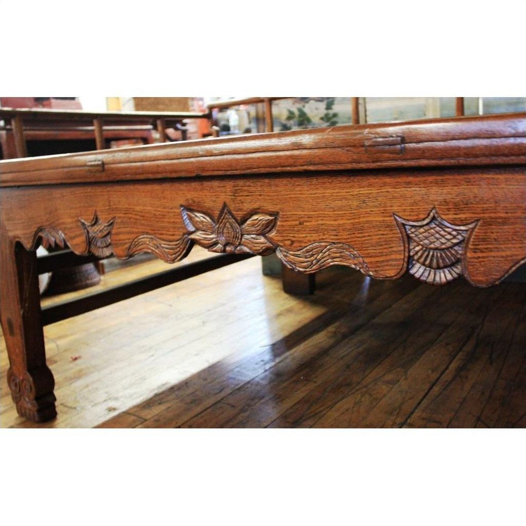 Close-up of dark wood Chinese daybed with carved floral and leaf patterns along the side, shown on a wooden floor.