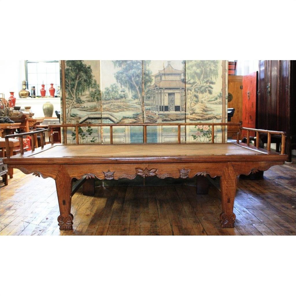 Dark wood Chinese daybed with carved legs, styled with Asian decor and a scenic Shanxi folding screen backdrop.