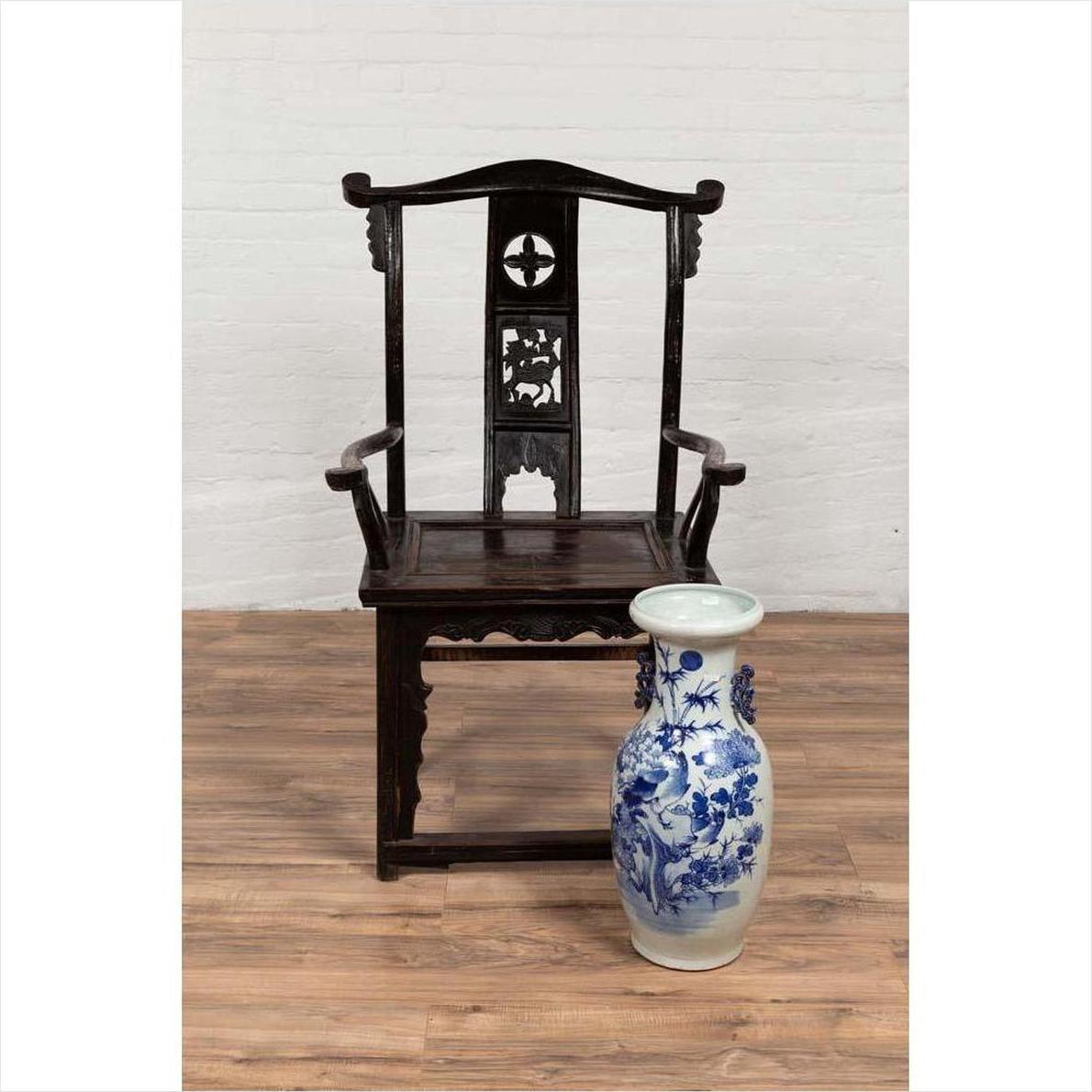 Dark patina Chinese elmwood Dengguayi scholar's chair behind tall blue-and-white porcelain vase on wood floor.