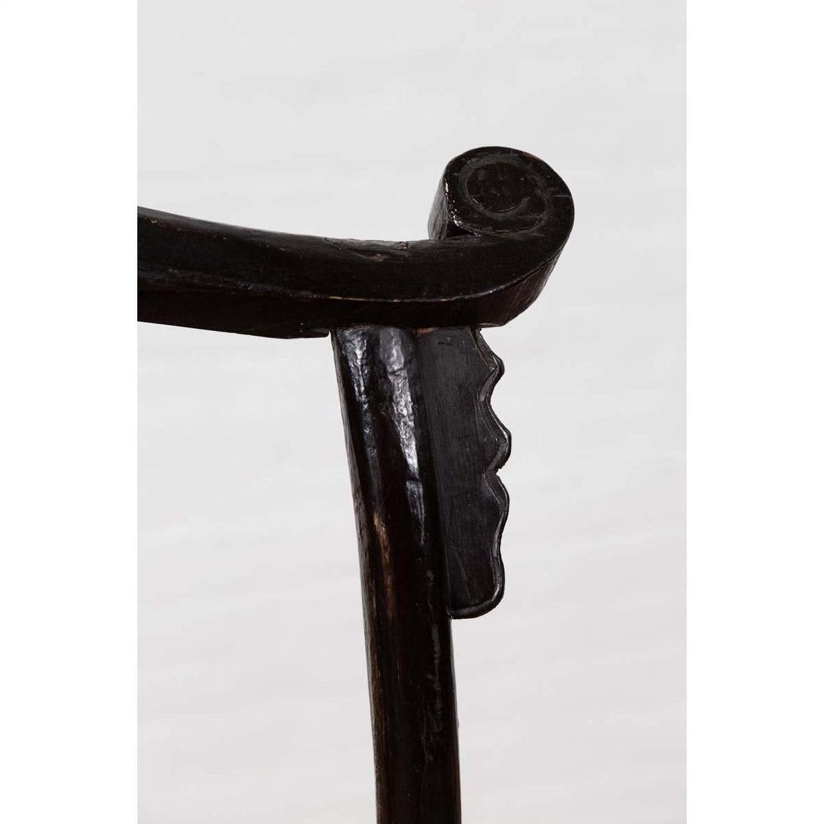 Close-up of dark Chinese elmwood armrest with curved notched design, Dengguayi Scholar's Chair, on light background.