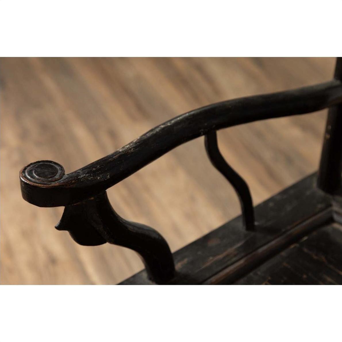 Close-up of dark patina Chinese elmwood chair armrest with curved carvings, blurred floor background.
