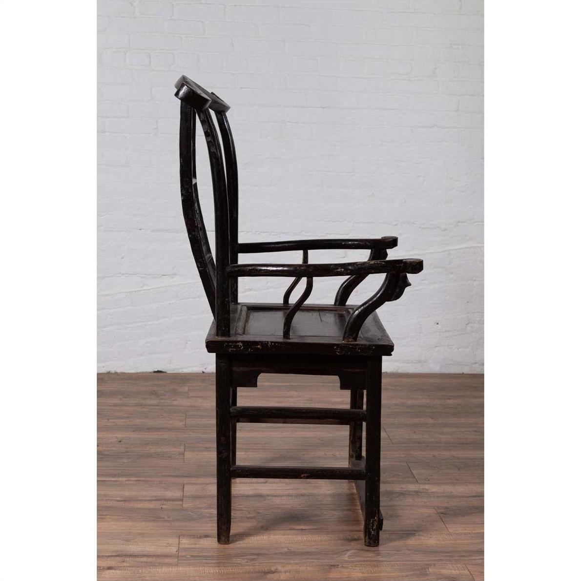 Dark wood Chinese elm chair, side view, on wooden floor with white brick wall in background.