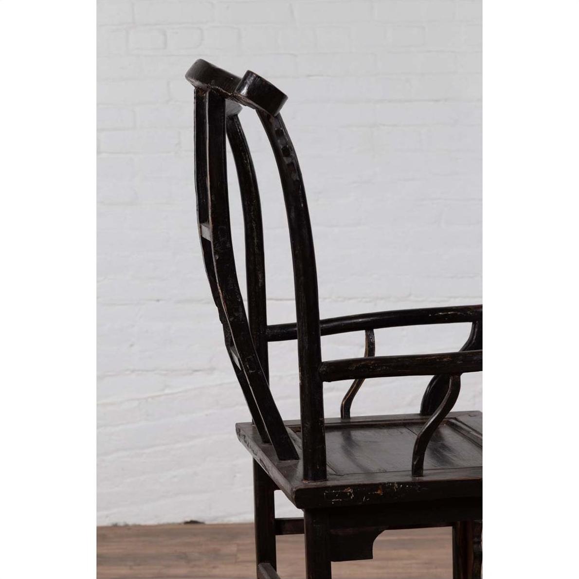 Dark wood Chinese elm chair, side view, on wooden floor with white brick wall background.