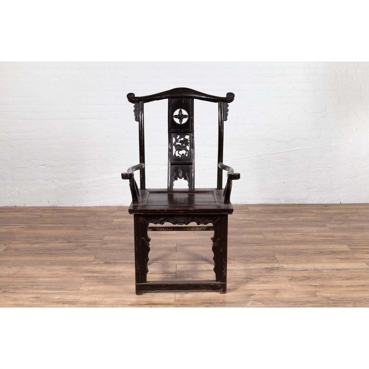 Dark patina elmwood scholar's chair with carvings on wood floor against white brick wall indoors.