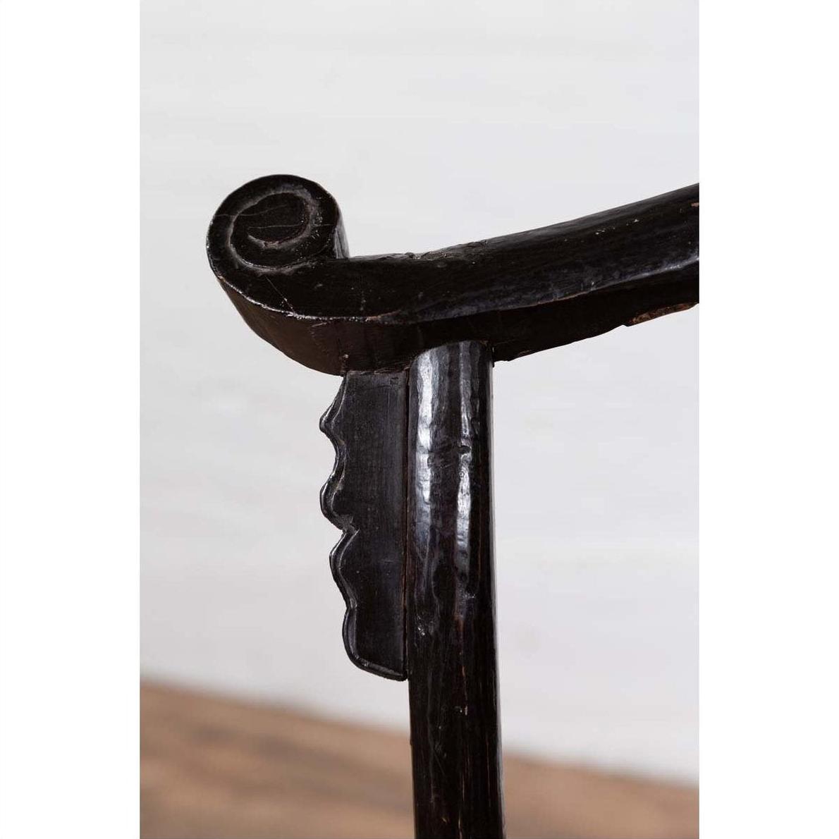 Close-up of dark patina elmwood chair scroll armrest, light background.
