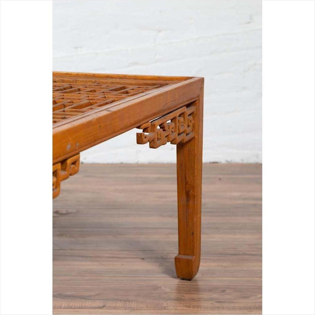 Close-up of a brown elmwood coffee table leg with horse-hoof feet and open fretwork, indoors against a white wall.