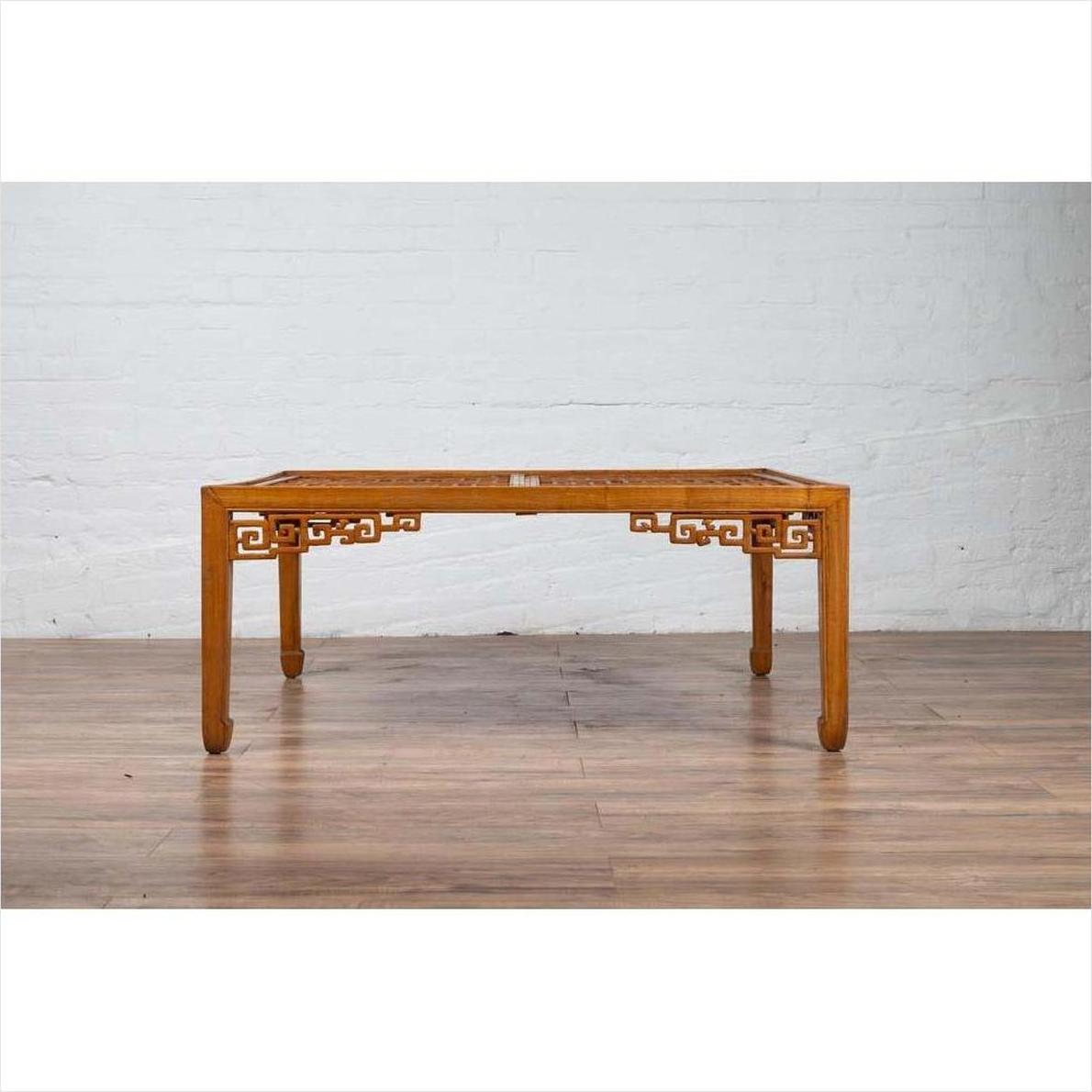 Brown elmwood square coffee table with open fretwork and horse-hoof legs against white brick wall on wood floor indoors.